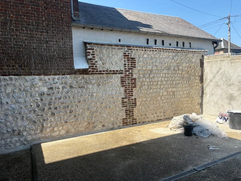 Mur en silex et brique avec travaux de maçonnerie en cours, sacs de matériaux au sol
